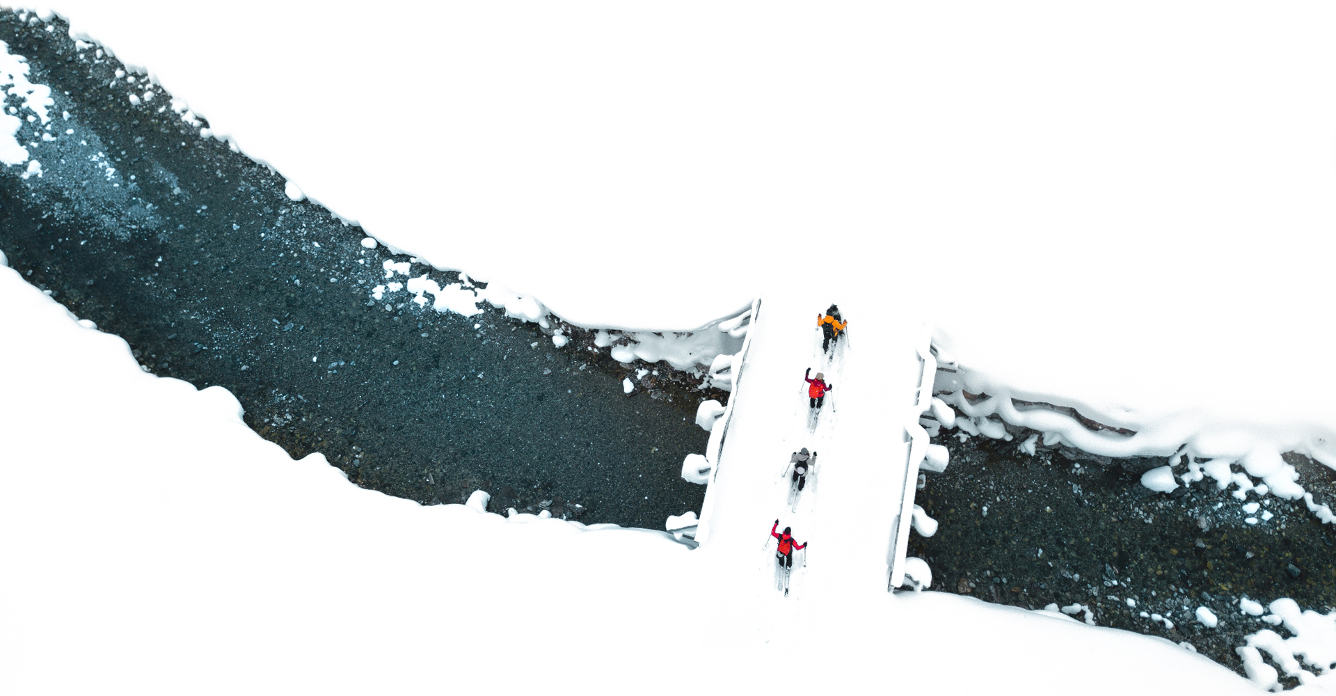 Grupa osób przejeżdzająca przez most nad rzeką na nartach skiturowych